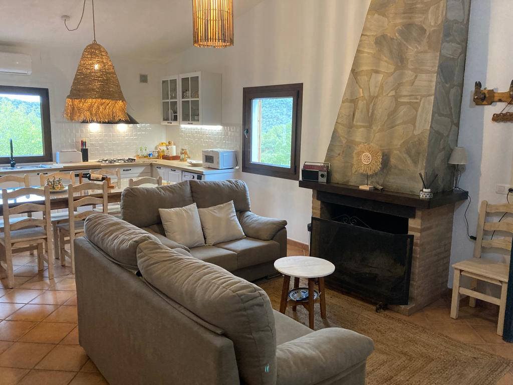Salón de la casa con chimenea, sofás y cocina abierta