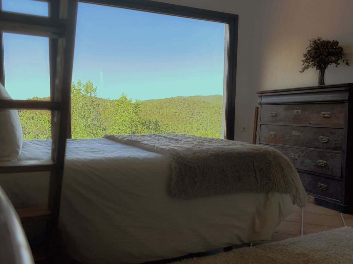 Cama de matrimonio frente al gran ventanal, con vistas al bosque